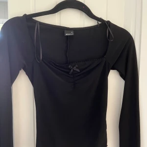 Svart långärmad topp från Gina Tricot - Snygg svart långärmad topp från Gina Tricot med en liten rosett framtill. Toppen har en elegant v-ringning.