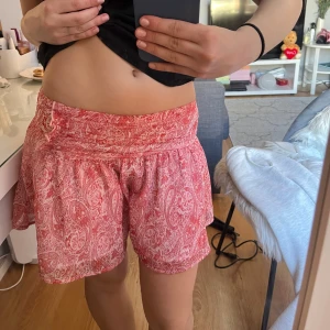 Röd och vit mönstrad kjol - Säljer en söt röd och vit kjol med paisleymönster. Kjolen har en volangdetalj och en bekväm passform. Perfekt för varma dagar!