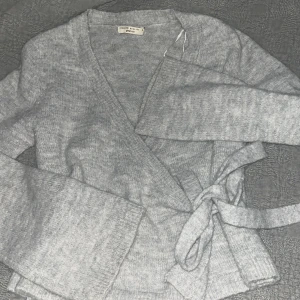 Omlott/knyt kofta  - Mysig grå omlottkofta från gina med knytband i midjan. Perfekt för kyliga dagar med sin mjuka och bekväma passform. Långärmad design som ger en stilren look.