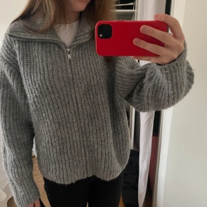 Grå stickad ribbad kofta med dragkedja - Ny med prislapp på! Säljer en mysig grå ribbad kofta med dragkedja och hög krage. Perfekt för kyliga dagar och enkel att matcha med olika outfits. Koftan har långa ärmar och en avslappnad passform.