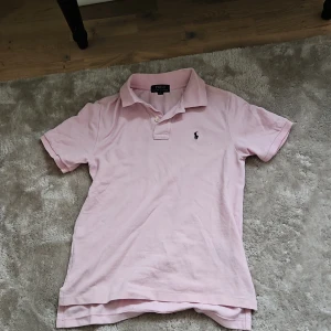 Rosa pikétröja från Ralph Lauren - Säljer en stilren rosa pikétröja från Ralph Lauren med klassisk krage och korta ärmar. Tröjan har den ikoniska broderade loggan på bröstet. Perfekt nu inför sommaren.