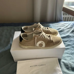 Beige sneakers från Oliver Cabell - Snygga beige sneakers från Oliver Cabell med vita och svarta detaljer. Skorna har en rund tå och snörning framtill. Perfekta för en stilren och avslappnad look.
