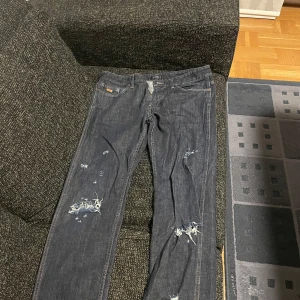 Mörkblå Hugo Boss jeans - Säljer ett par mörkblå Hugo Boss jeans med coola slitningar på framsidan. De har en klassisk femficksdesign och en läderpatch på baksidan. Perfekta för en avslappnad stil.