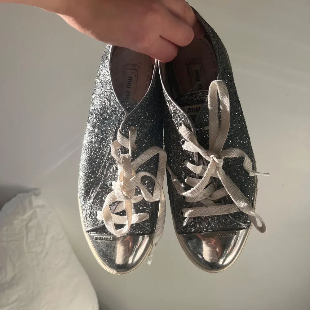 Snygga glittriga sneakers från Miu Miu med silverfärgade detaljer och snörning. Perfekta för att ge din outfit en extra touch av glamour. Skorna har en rund tå och är dekorerade med ett glittrigt mönster. Skriv för fler bilder💕 kartong ingår ej!. Kengät.