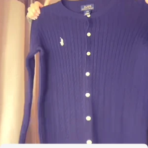 Blå kofta från Polo Ralph Lauren - Säljer en snygg blå kofta från Polo Ralph Lauren med ribbad struktur och vita knappar. Den har långa ärmar och en liten logga på bröstet. Perfekt för en stilren look.