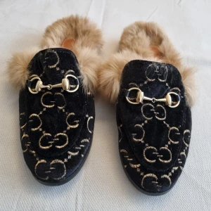 Svarta loafers med päls och metallspänne - Snygga svarta loafers med pälsfoder och dekorativa metallspännen. Skorna har ett broderat tyg i sammet.