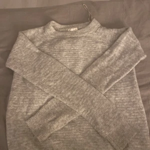 Grå stickad tröja från Cubus  - Mysig grå stickad tröja från Cubus. Perfekt för kyliga dagar med sin mjuka och bekväma passform. Tröjan har långa ärmar och en klassisk rund halsringning.