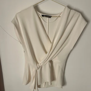 Vit omlottopp från Zara - Säljer denna populära vita omlottopp från Zara med knytning framtill. Den är använd Max 3 gånger och har väldigt bra skick!💕