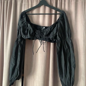 Svart croppad blus med knyt - Snygg svart croppad blus med långa ärmar och knytning framtill. Perfekt för en trendig look.