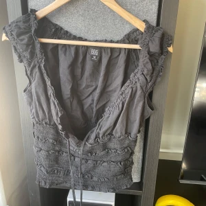 Grå topp från BDG - Säljer en snygg grå topp från BDG med volangdetaljer och knytning framtill. Den är elastisk vid midjan.