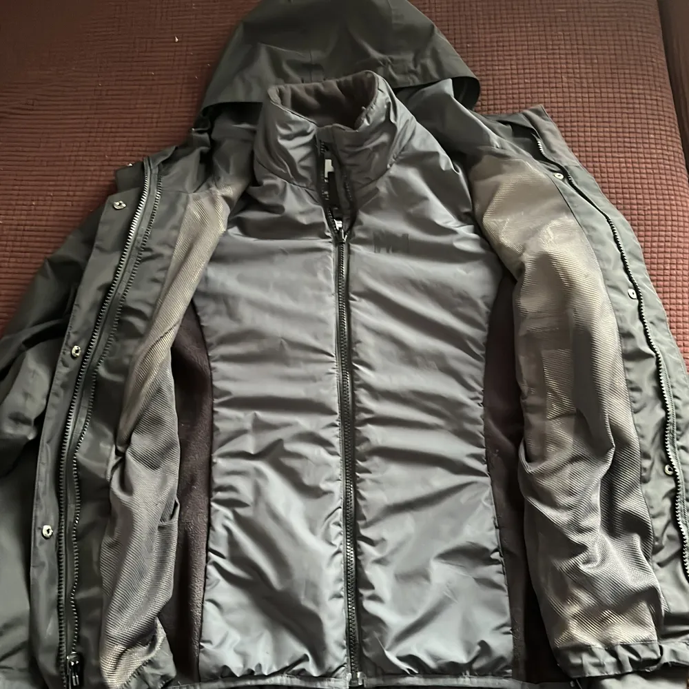 Säljer en svart jacka från Helly Hansen med huva och dragkedja. Jackan har en stilren design och är perfekt för kyligare väder. Den är i storlek XS och har en innerjacka som kan bäras separat.. Takit.