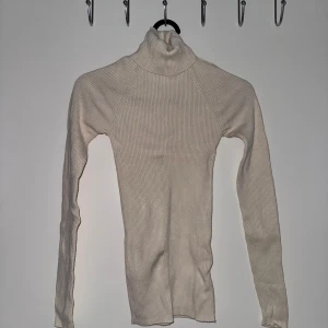 Beige ribbad polotröja från Gina Tricot - Aldrig använd! Säljer en stilren beige polotröja från Gina Tricot. Tröjan är ribbad och har långa ärmar, perfekt för kyligare dagar. Den mjuka polokragen ger extra värme och stil. Passar utmärkt till både jeans och kjol. 🧥✨