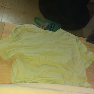 Baby grön t-shirt från H&M - Säljer en baby grön t-shirt från H&M i ekologisk bomull. Den har en broderad text 'New York City' på bröstet. Perfekt för en avslappnad stil.