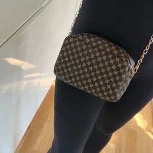 Mönstrad axelväska med kedja - Snygg axelväska med ett elegant mönster i brunt och beige. Väskan har en praktisk dragkedja och en stilren kedja som axelrem. Perfekt för att bära dina nödvändigheter med stil. Aldrig använd 