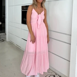 Ny! Rosa långklänning med knyt - Ny med lappar kvar! Säljer en söt rosa långklänning med knyt framtill. Klänningen har en ärmlös design och en luftig passform, perfekt för varma dagar. Den har en feminin och romantisk stil som passar bra till sommarens alla tillfällen. Från DesignBySi