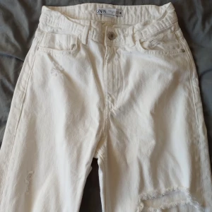 Vita jeansbyxor från Zara - Snygga vita jeansbyxor från Zara med slitna detaljer. Byxorna har en hög midja och en rak passform som ger en trendig look. Perfekta för att skapa en stilren outfit med en avslappnad känsla.