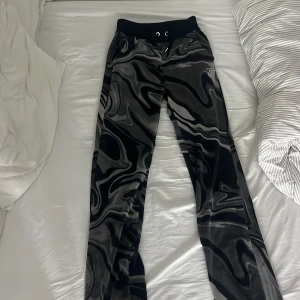 Svarta mjukisbyxor från Juicy Couture - Snygga svarta mjukisbyxor från Juicy Couture med ett unikt mönster och glittrande Juicy-logga på baksidan. Byxorna har en bekväm resårmidja med snörning för perfekt passform. Dock så är en liten ”plupp” på knytbanden vid midjan borta. Men annars i väldigt bra skick. 