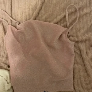 Glittrig rosa linne - Säljer ett glittrigt rosa  linne med smala axelband. Perfekt för en kväll ute eller en festlig tillställning. Linnet har en enkel och stilren design som gör det lätt att matcha med olika outfits.