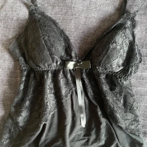 Svart spetslinne med rosett - Säljer ett svart linne med spetsdetaljer och en söt rosett framtill. Linnet har smala axelband och en vacker spetsdesign. Lappen är borta men storken är xs och den är från new Yorker🩷