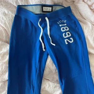 Abercrombie & Fitch byxor - Snygga blå mjukisbyxor från Abercrombie & Fitch med vit snörning i midjan och tryck 'Fitch 1892' på benet. Perfekta för en avslappnad stil.