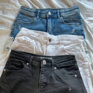 Tre par shorts i olika stilar - Säljer tre par shorts: ett par svarta shorts i jeansmaterial, ett par vita shorts i jeans och ett par blå jeansshorts med spetsdetaljer. Perfekta för sommaren och olika tillfällen.