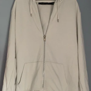 Vit huvtröja från The Black Label Collection - Säljer en stilren vit huvtröja från The Black Label Collection. Tröjan har en dragkedja framtill och en bekväm huva. Perfekt för en avslappnad look.