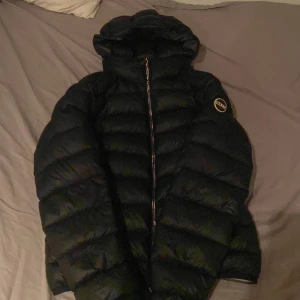 Svart dunjacka från Colmar - Säljer en svart dunjacka från Colmar med huva och dragkedja. Jackan har en puffig design och ett märke på ärmen. Perfekt för kalla dagar! Det är inte fläckar det är bara ljuset på dom två första bilderna. Dragkedjan går upp ibland men det är bara att dra ner den lägsta. Det är storlek 40/xxs/xs. Skriv om ni vill ha bild på QRkoden elr andra frågor!