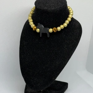 Guldglittrigt armband med dalahäst - Snyggt armband med glittriga guldfärgade pärlor och en svart dalahäst. Perfekt för att ge en unik touch till din stil.