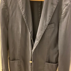 Mörkblå tunn kavaj från Santaniello - Elegant mörkblå kavaj från Sanataniello. Klassisk design med tre knappar framtill och fickor. Perfekt för formella tillfällen.