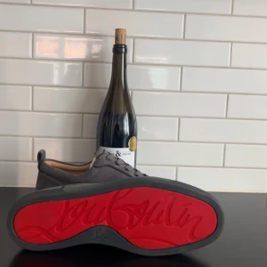 Grå sneakers från Christian Louboutin - Snygga grå sneakers i mocka från Christian Louboutin med den ikoniska röda sulan. Skorna har snörning och en stilren design som passar perfekt för en trendig look.