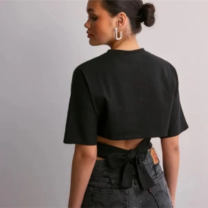 Svart knyttopp från Nelly  - Snygg svart croppad topp med korta ärmar och knytning i ryggen. Perfekt för en trendig look. Köpt från Nelly, använd en gång. Säljer pga för liten. 