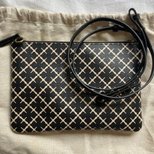 By Malene Birger väska  - Snygg axelväska från By Malene Birger i svart och beige med ett stilrent geometriskt mönster. Väskan har en justerbar axelrem och en dragkedja för säker förvaring. Perfekt för att ge din outfit en elegant touch. Kommer med i original påsen och bandet till den är hyfsat ny nästan aldrig använd 