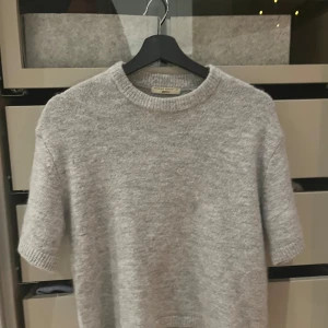 Grå stickad tröja från Gina Tricot - Mysig grå stickad tröja från Gina Tricot i premiumkvalitet. Tröjan har en rund halsringning och trekvartsärmar, perfekt för kyligare dagar. Enkel och stilren design som passar till det mesta.