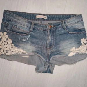 Jeansshorts med blommig spets - Snygga jeansshorts med blommig spetsdetalj på sidorna. De har en klassisk blå jeansfärg och är lågmidjade. Perfekta för en somrig look! Köpta här på Plick men passade ej mig, första två bilderna är lånade💗skulle säga att de även passar S