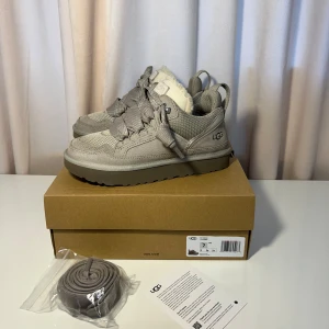 UGG Lowmel - Snygga grå sneakers från UGG med snörning och mjukt foder. Skorna har en robust sula och är perfekta för kyligare dagar. De har en stilren design med UGG-loggan på sidan.