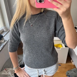 Grå trekvartsärmad stickad tröja - Säljer en stilren grå stickad tröja med trekvartsärm. Perfekt för en avslappnad look. Tröjan har en rund halsringning och är gjord i ett mjukt material som känns skönt mot huden.