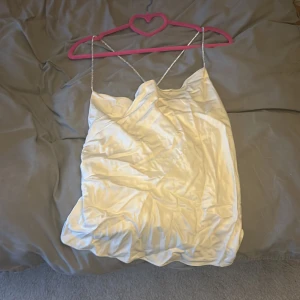 Vit siden tröja från H&M - Säljer en elegant vit siden tröja från H&M med tunna glittriga axelband. Perfekt för en stilren look. Tröjan har en mjuk och glansig yta som ger en lyxig känsla. Passar bra till både fest och speciella tillfällen. 💫