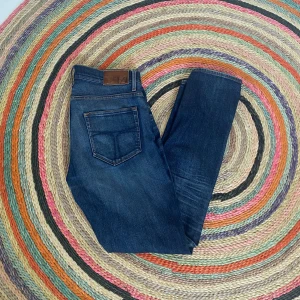 TOS JEANS - Snygga mörkblå jeans med en klassisk femficksdesign och knappgylf. Perfekta för en avslappnad stil. De har en lätt tvättad look som ger en cool vibe.