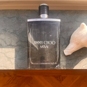 Jimmy Choo Man Parfym - Säljer en stilren och maskulin parfym från Jimmy Choo. Flaskan är elegant med en mörk tonad glasdesign och en svart kork med silverdetaljer. Perfekt för den moderna mannen som vill ha en fräsh sommar doft. Flaskan har förvarats i en mörk och sval plats större delen av tiden. Anledningen till att flaskan är lite sönder här och där är p.g.a att jag hade den i min rygga några gånger. Men parfymen är det inget fel på!