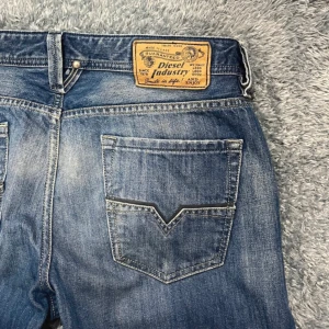Blå jeans från Diesel - Snygga blå jeans från Diesel med klassisk femficksdesign och en cool tvättad look. De har en knappgylf och en läderpatch med Diesel-logga på baksidan. Perfekta för en avslappnad stil. Skriv vid frågor! 