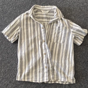 Randig kortärmad skjorta från H&M (perfekt för sommaren (billigare vid snabb affär)) - Säljer en stilren randig skjorta från H&M i storlek 146. Skjortan har korta ärmar och knappar framtill. Perfekt för en avslappnad look med sina blå och vita ränder. Den har en bröstficka för extra stil och funktionalitet.