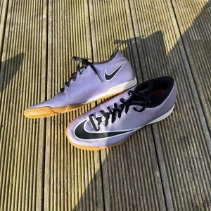 Lila fotbollsskor från Nike inomhus skor - Snygga lila fotbollsskor från Nike med svart snörning och vit sula. Perfekta för spel på planen med sin smidiga design och greppvänliga sula.