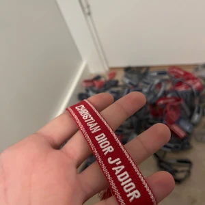 2 styckenChristian Dior J'Adior armband - Snygga armband från Christian Dior med texten 'J'Adior'. Finns i både rött och svart med vit brodyr. Perfekt accessoar för att lyfta din outfit och visa din stil. Justerbar passform med tofsar i ändarna. Ikonisk och trendig detalj för dig som gillar lyxiga märken.