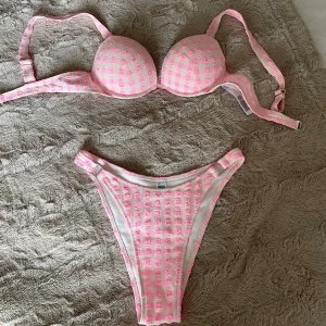 Rutig rosa och vit bikini - Superfin bikini med vadderad bygel-bh och högt skurna trosor. Mönstret är rutigt i rosa och vitt, vilket ger en söt och trendig look. Perfekt för stranden eller poolen i sommar! Justerbara axelband för bästa passform.