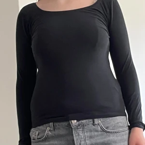 Svart långärmad topp från 157 - En svart, figurnära långärmad topp från 157 i storlek S. Tillverkad i mjuk bomull med lite stretch för en bekväm passform. Enkel och stilren design med rundad halsringning, perfekt att matcha med jeans eller kjol.