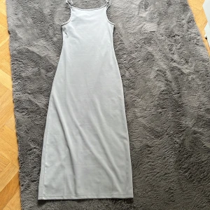 Ljusgrå långklänning - Enkel och stilren ljusgrå långklänning från 157 med smala axelband och rak passform. Klänningen är ärmlös och har en minimalistisk look som passar perfekt till sommaren. 