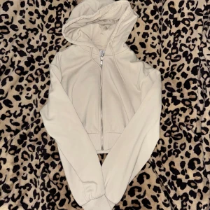 Vit cropped tjocktröja från H&M - Säljer en vit tjocktröja med dragkedja framtill och huva med snörning. Tjocktröja  är croppad och har långa ärmar med breda muddar. Den är aldrig använd bara provad.