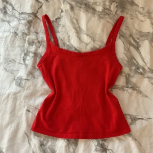 Röd linnetopp med smala axelband - En enkel och snygg röd linnetopp med smala axelband och rak halsringning. Toppen är figurnära och passar perfekt till jeans eller kjol. Mjuk och stretchig känsla, perfekt för varma dagar.
