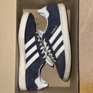 Adidas Gazelle - Säljer ett par klassiska Adidas Gazelle sneakers i marinblå mocka med vita detaljer och guldtext på sidan. Det följer även med blåa snören.