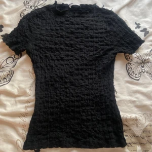 Svart ribbad topp från Zara - Säljer denna svarta t-shirt från Zara i storlek S som har ett stretchigt material med textur på